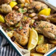 Close-up view of golden roasted chicken, tender potatoes, red onion, and bright lemon wedges in a sheet pan dinner.