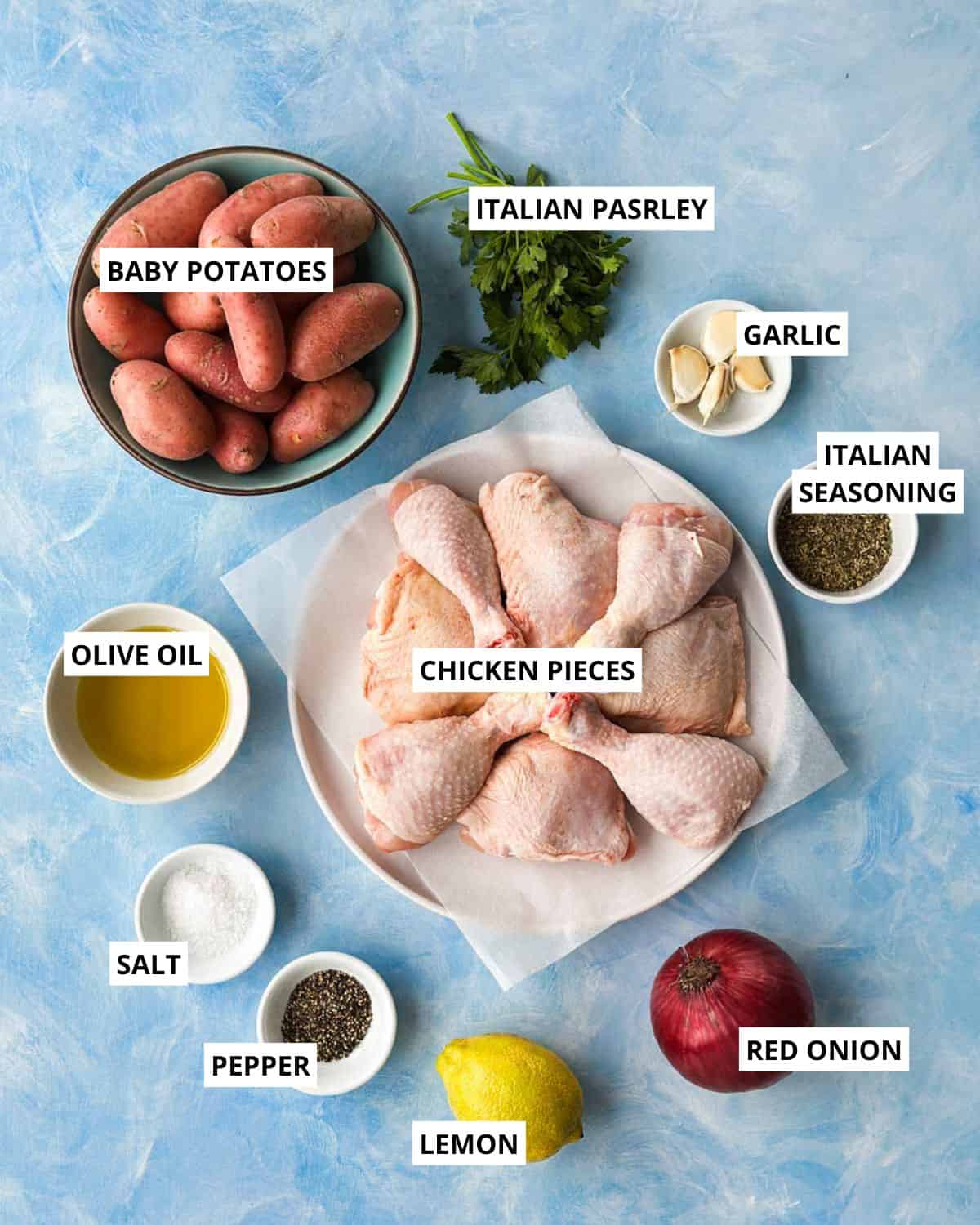 Overhead ingredient layout for sheet pan chicken and potatoes with chicken pieces, baby potatoes, lemon, garlic, herbs, and olive oil.