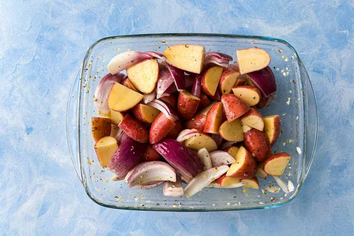 Baby potatoes and red onion tossed with Italian herb marinade in a glass baking dish.