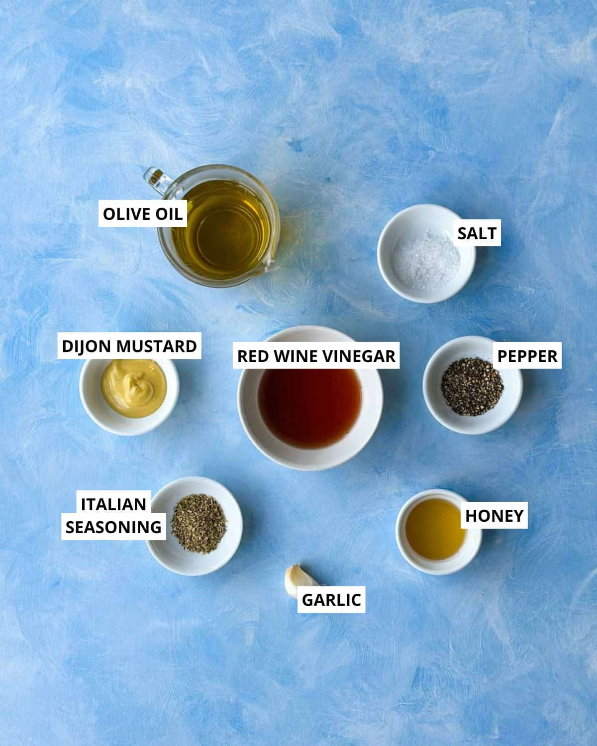 Top view of Italian vinaigrette ingredients including olive oil, red wine vinegar, Dijon, garlic, honey, and herbs.