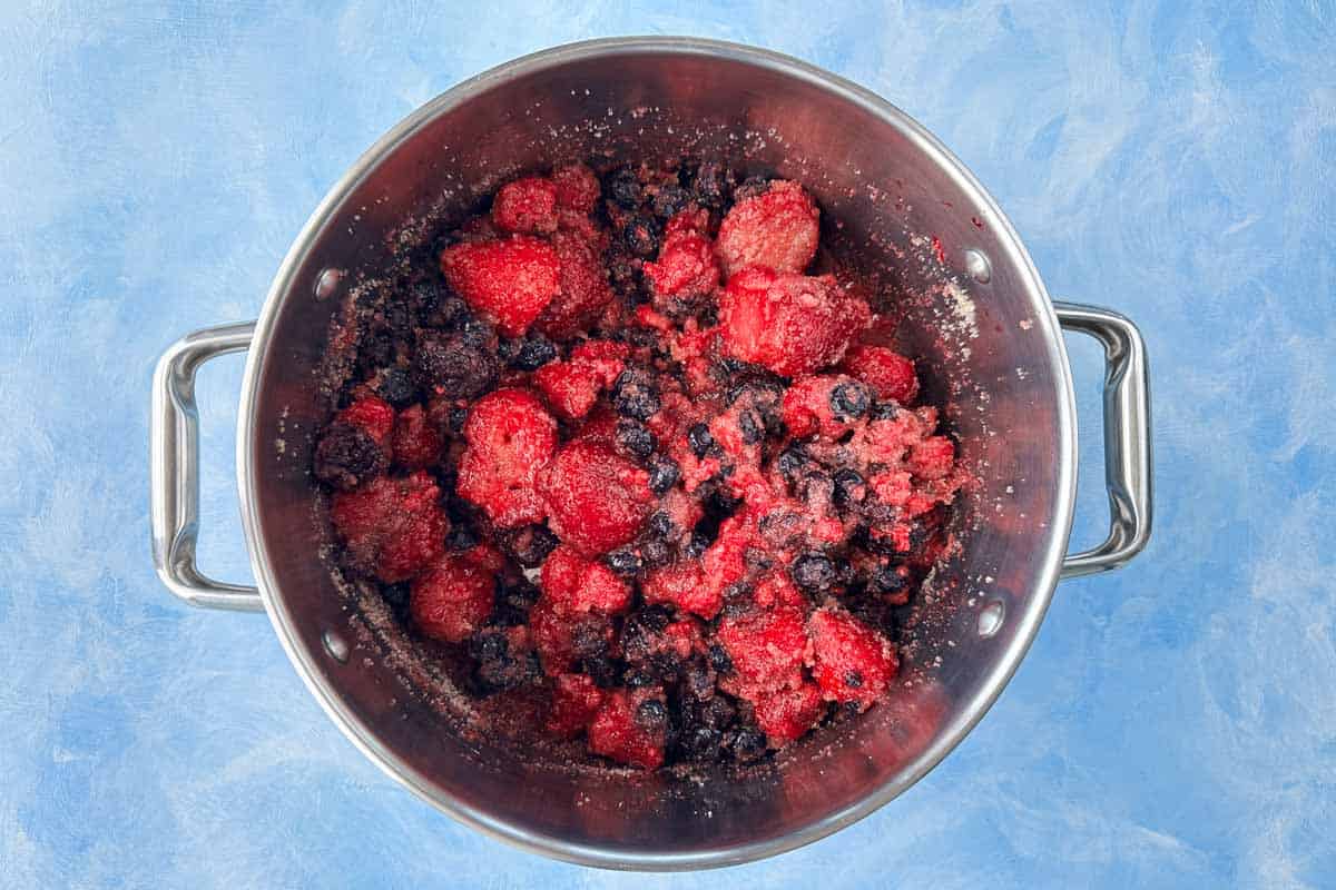 Frozen mixed berries and sugar added to a stainless steel pot before cooking into jam.