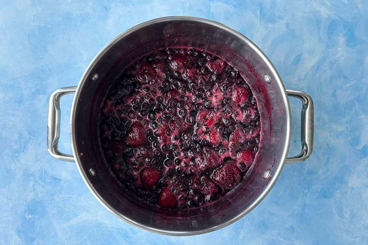 Mixed berries simmering in a pot as the fruit softens and releases deep red-purple juices.