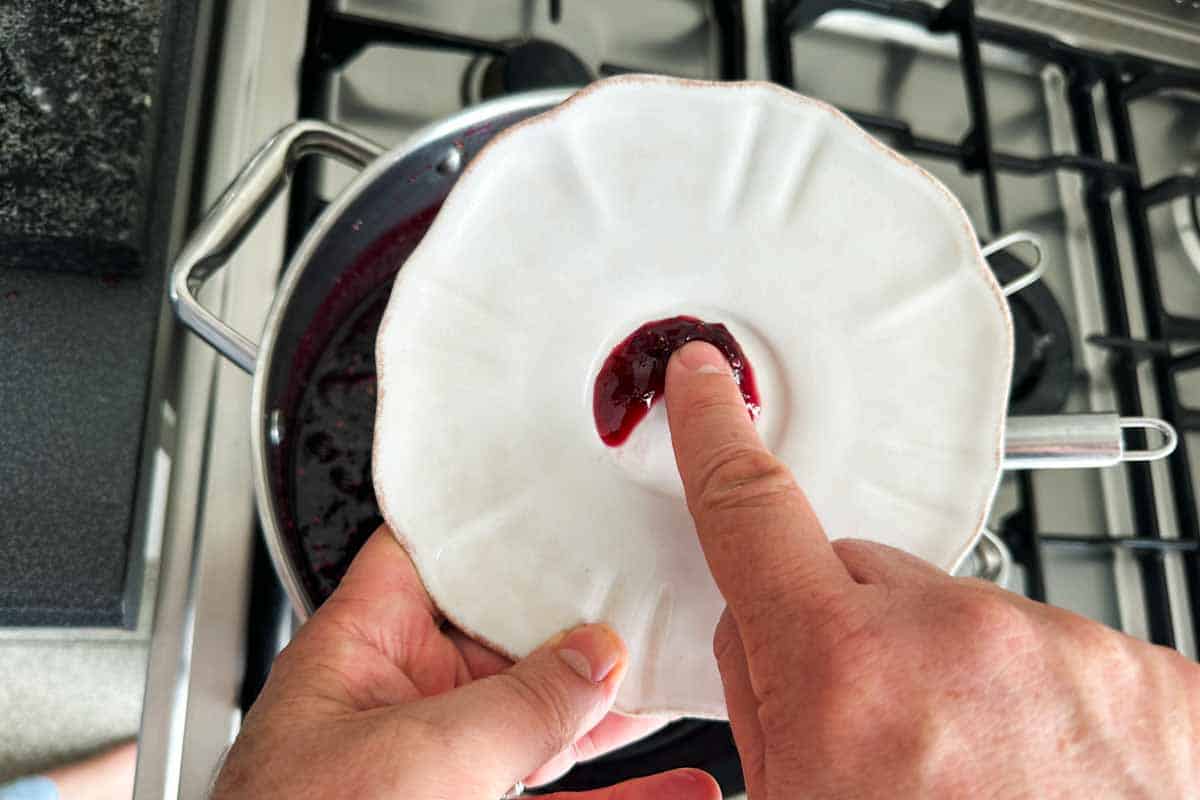 Testing mixed berry jam on a chilled plate to check if it wrinkles and sets properly