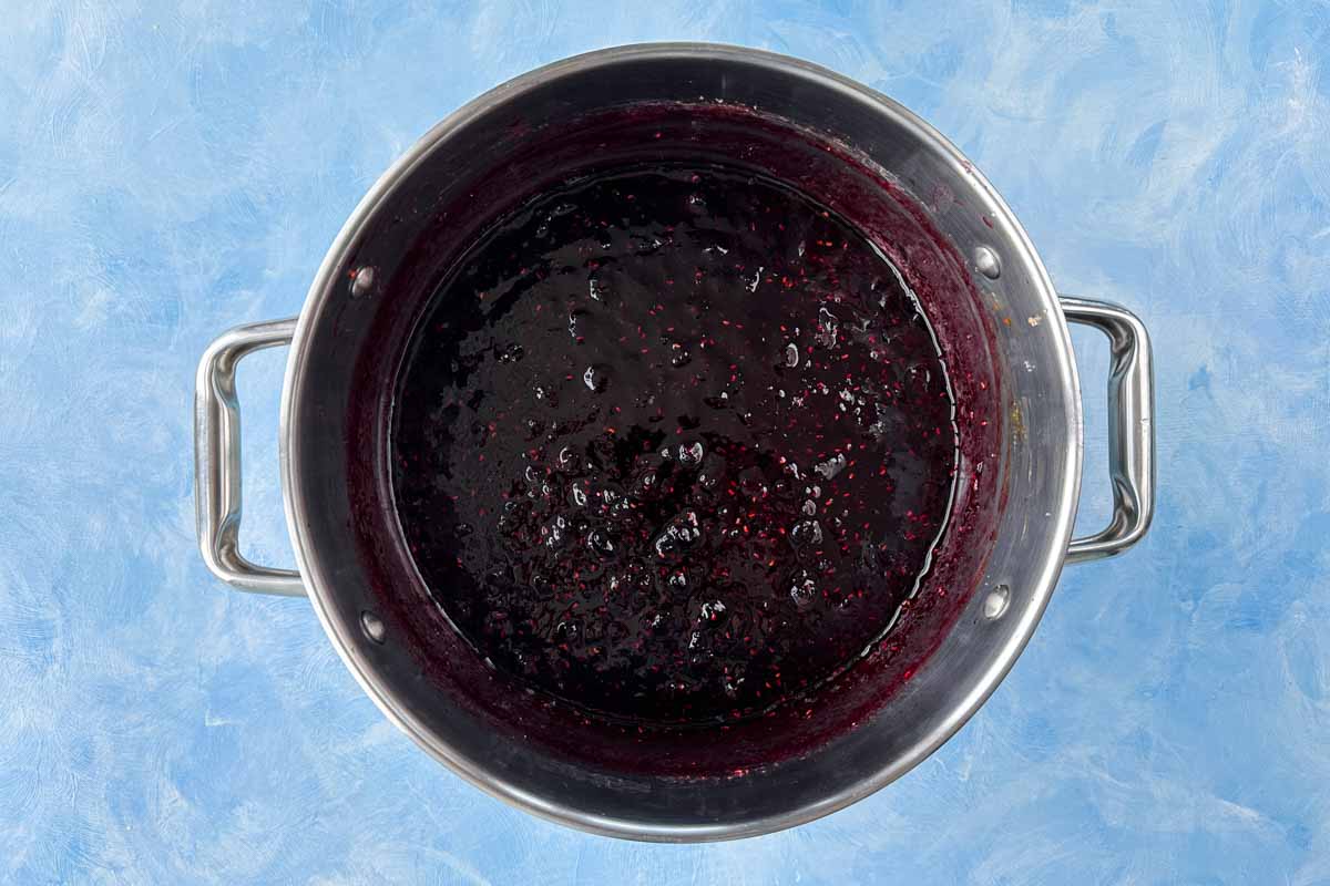 Thickened mixed berry jam in a pot with a glossy texture and visible berry seeds after cooking.