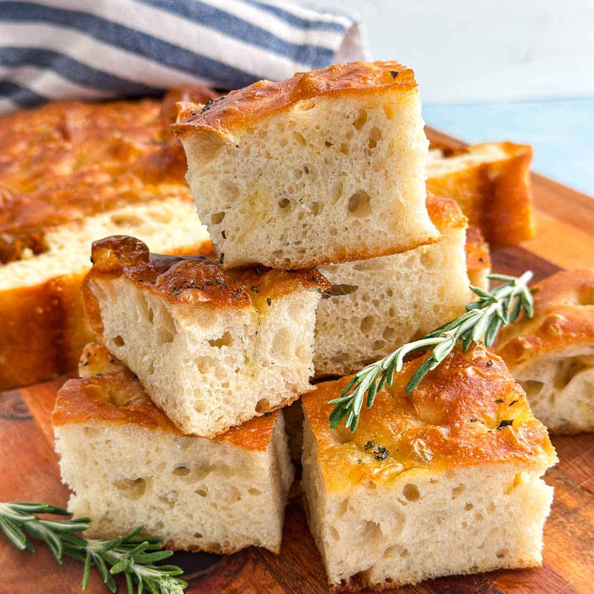 Close-up of thick focaccia bread pieces with golden olive oil crust, airy texture, and rosemary garnish.