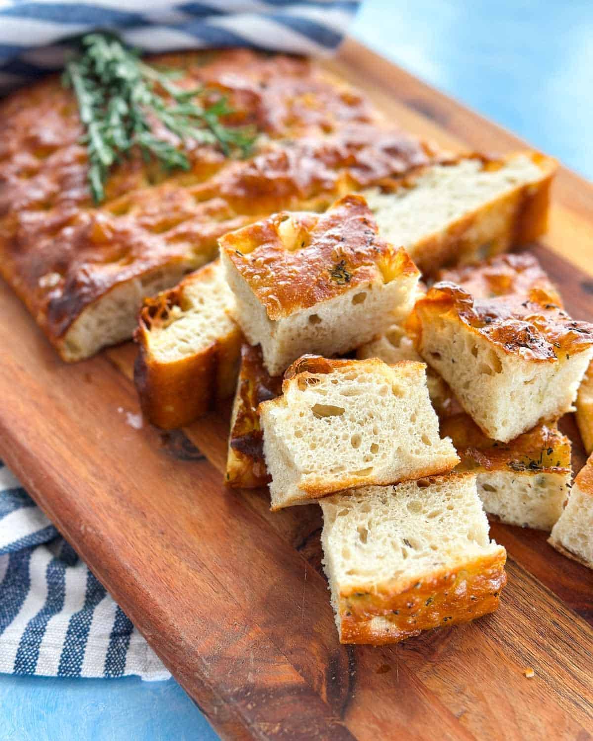 Focaccia bread pieces with a crisp golden top and soft open crumb arranged on a wooden board.