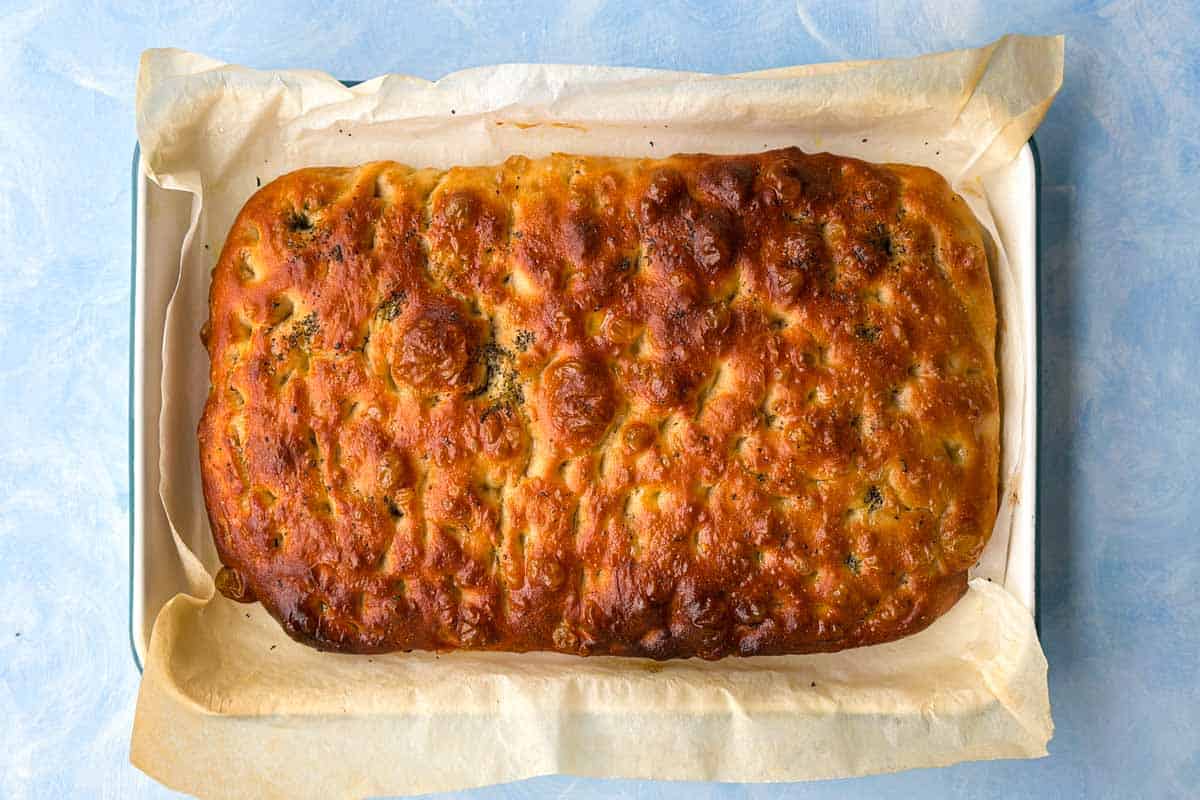 Freshly baked focaccia bread with a deep golden crust, rosemary, and crisp dimpled edges in the baking dish