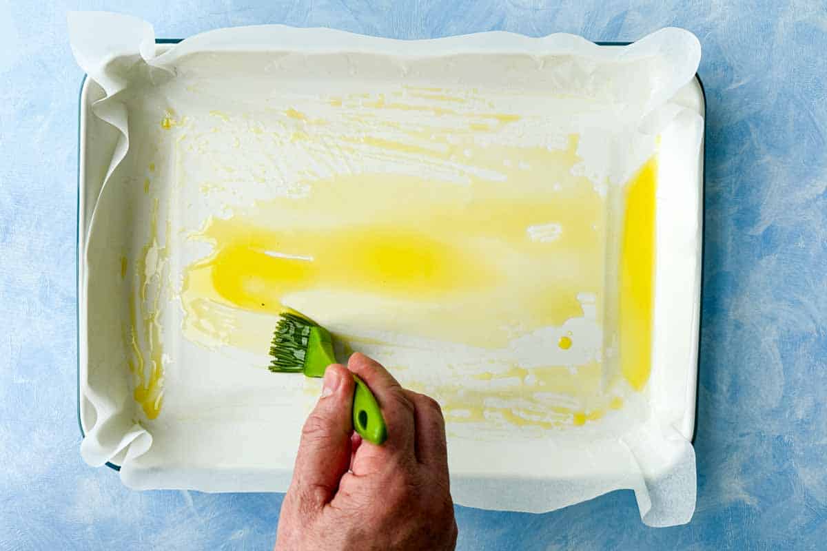 Brushing olive oil over a parchment-lined baking dish before adding the focaccia dough.