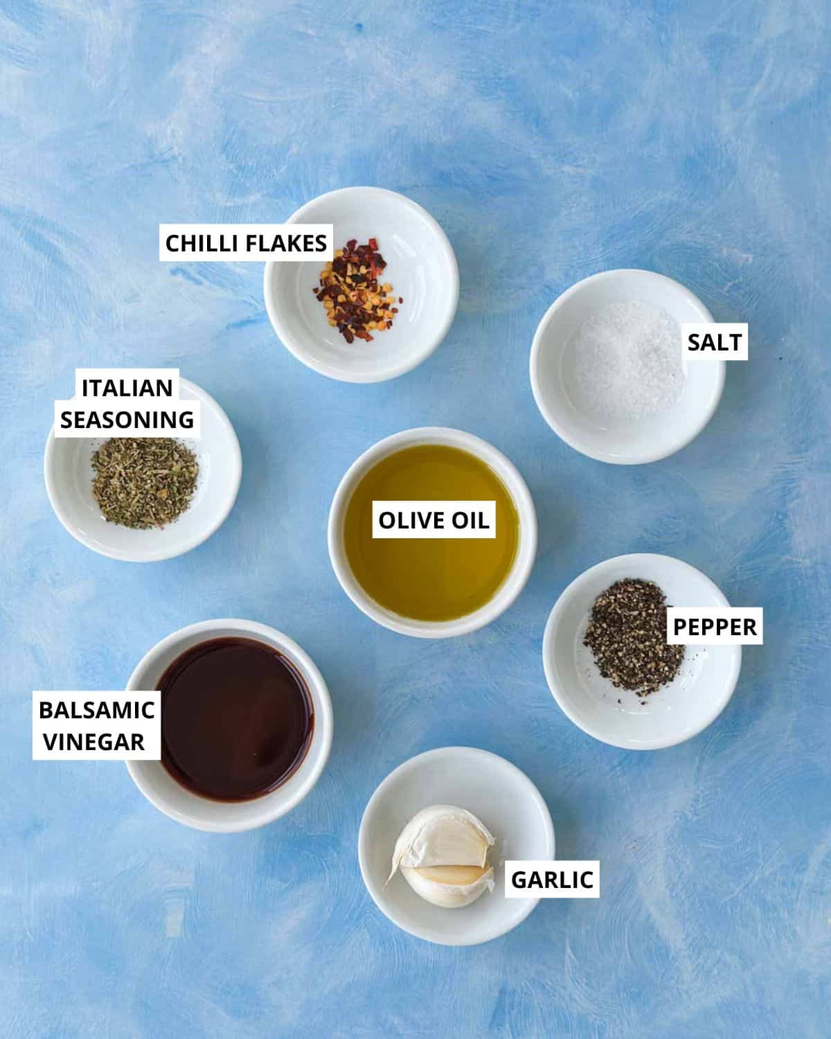 Ingredients for olive oil bread dip including olive oil, balsamic vinegar, garlic, Italian seasoning, chilli flakes, salt, and pepper
