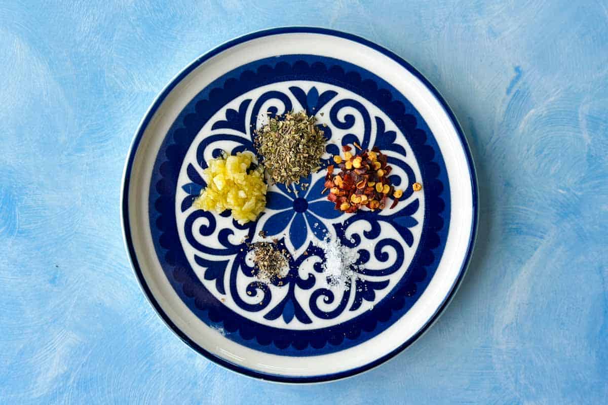 Minced garlic, Italian seasoning, chilli flakes, salt, and black pepper arranged on a decorative plate for olive oil bread dip