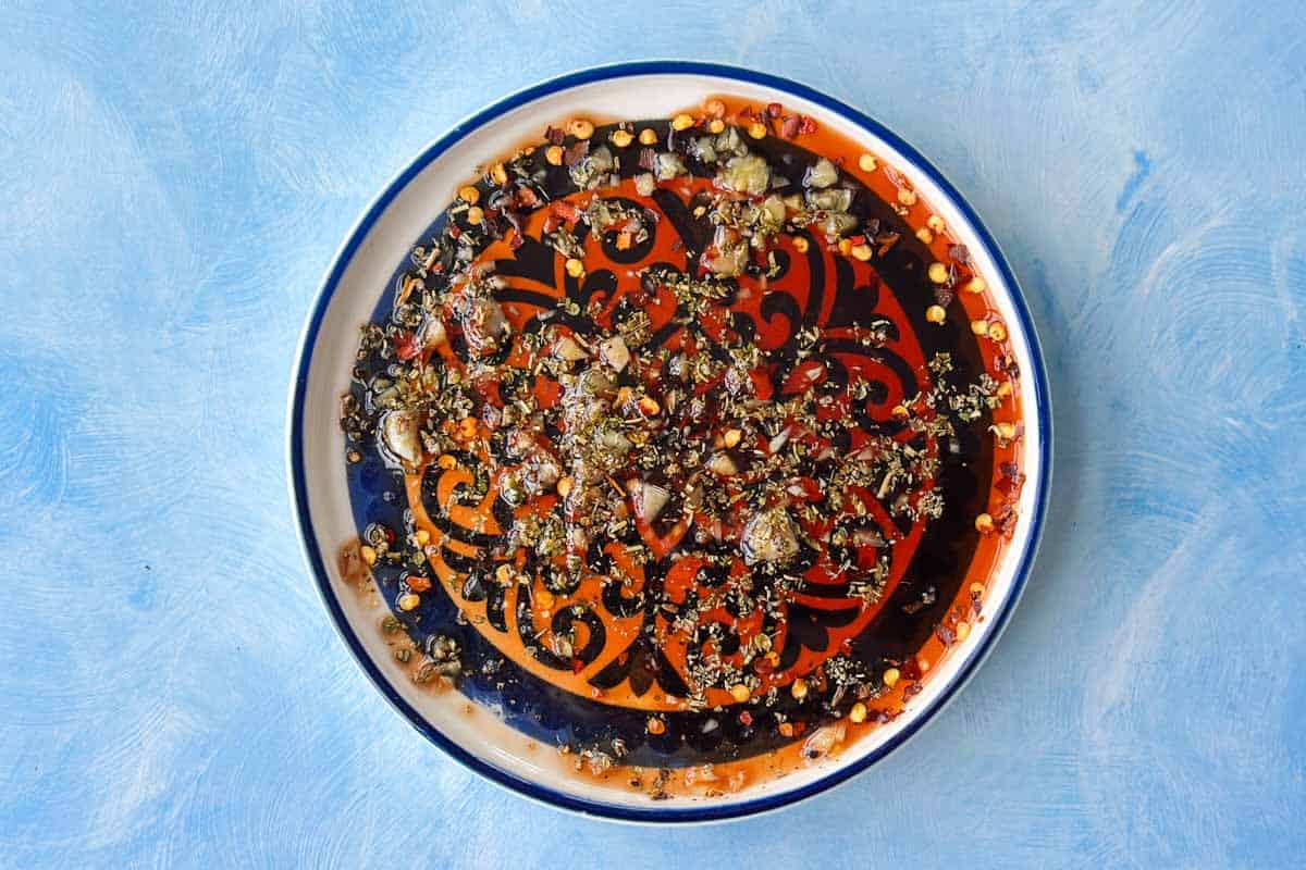 Olive oil bread dip mixed with balsamic vinegar, garlic, chilli flakes, and Italian herbs in a shallow serving bowl