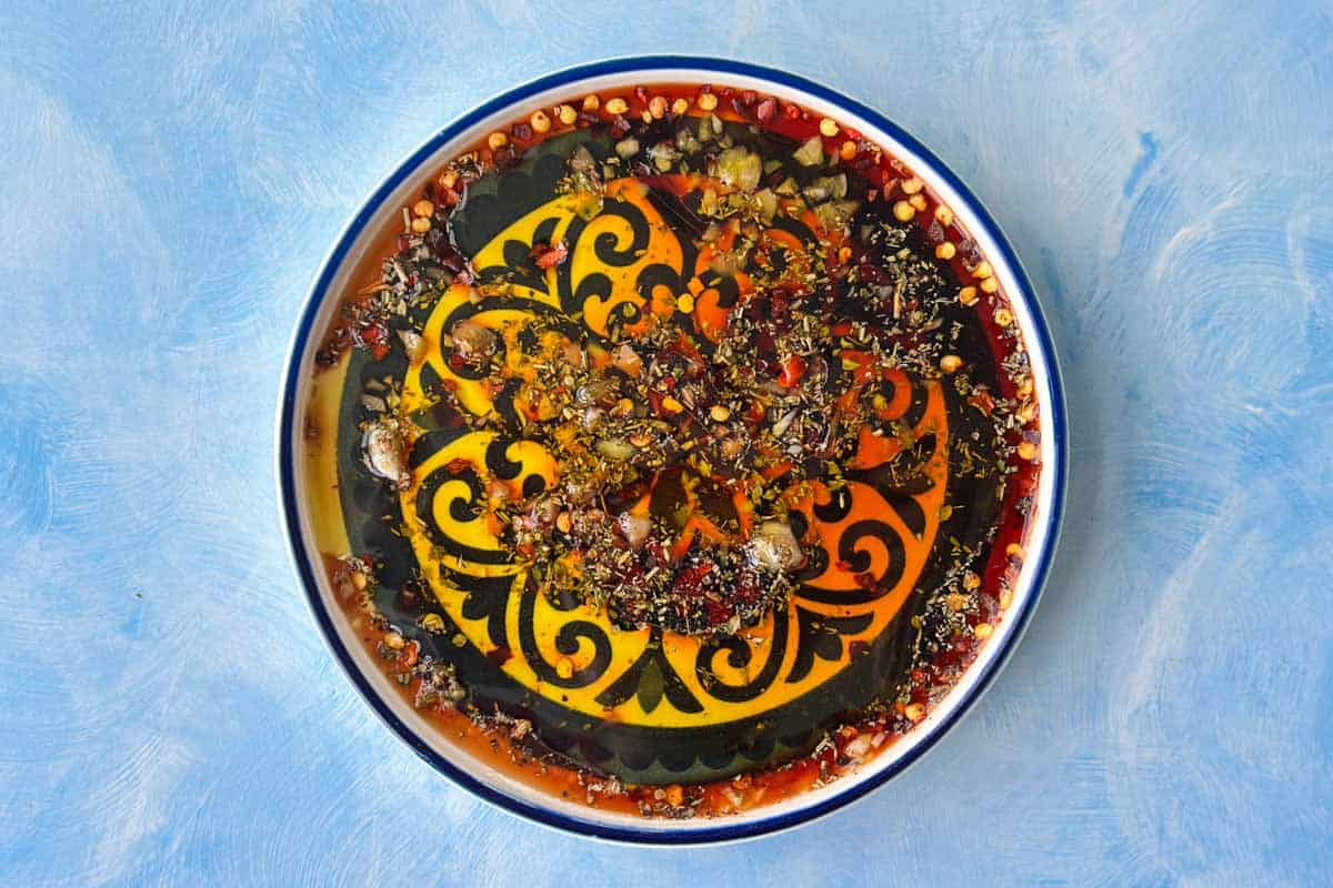 Overhead shot of olive oil bread dip with olive oil, balsamic vinegar, garlic, herbs, and chilli flakes ready for serving