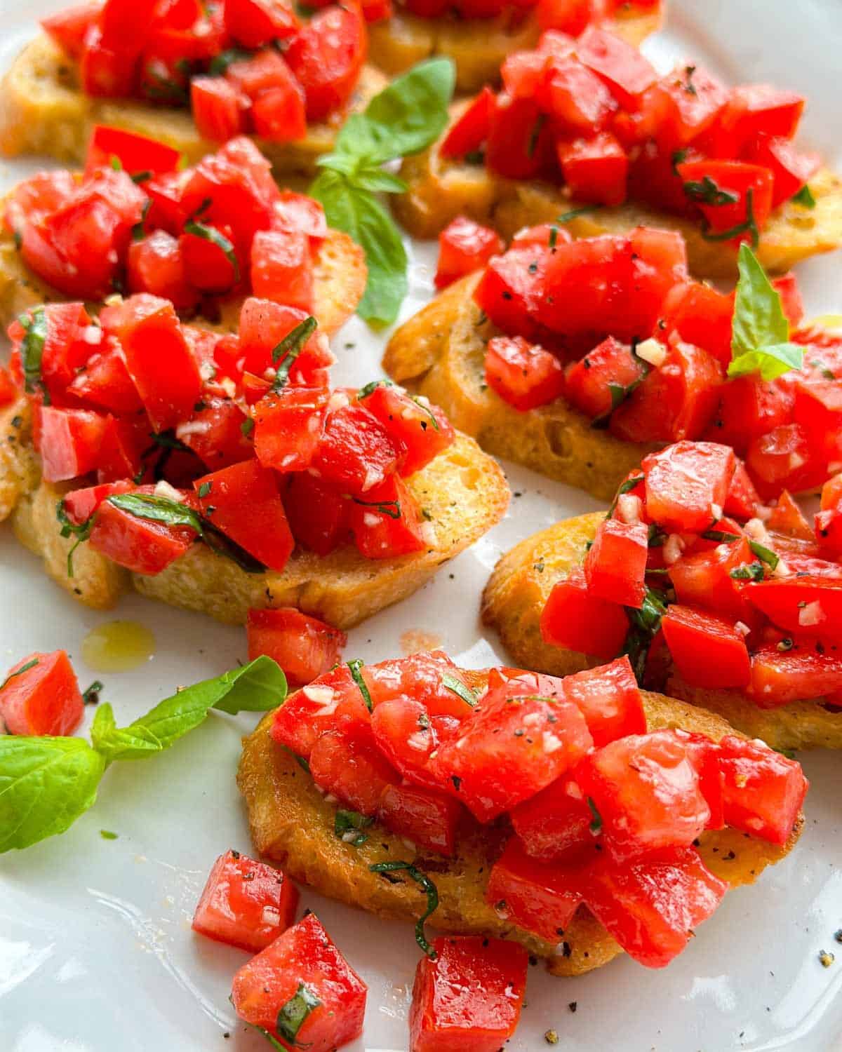 Close-up angled image of fresh tomato bruschetta crostini topped with juicy chopped tomatoes, basil ribbons, garlic, and olive oil on golden toasted baguette slices.