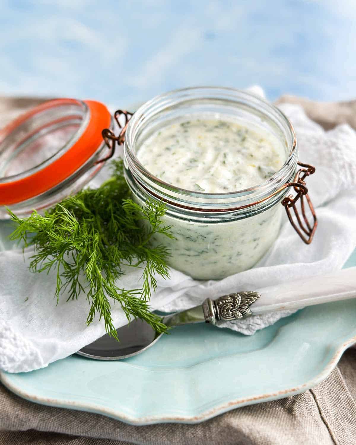 Side view of creamy herb dressing with Greek yogurt, fresh dill, and herbs served in a glass jar.