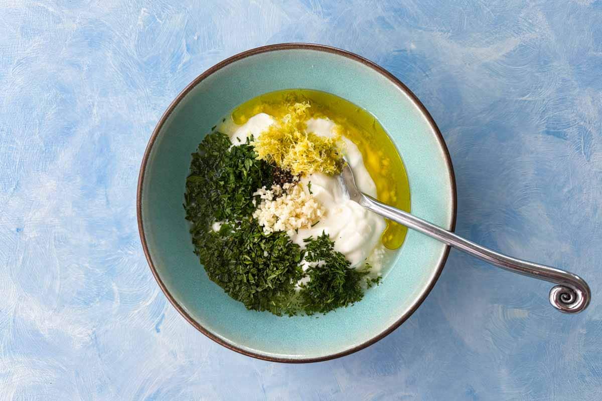Greek yogurt, fresh herbs, garlic, lemon zest, olive oil, salt, and pepper combined in a bowl before mixing.