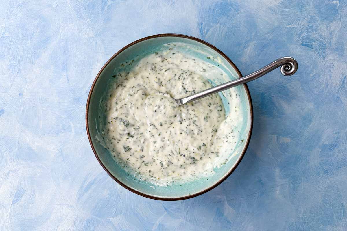 Top-down view of creamy herb dressing mixed until smooth and thick with finely chopped fresh herbs.