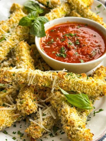 Close-up of crispy zucchini fries with Parmesan and basil, served with a bowl of spicy Arrabbiata Sauce.
