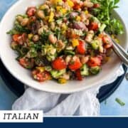 Colorful dense bean salad with vegetables and herbs in a white bowl.