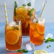 Refreshing lemon iced tea with slices of lemon and mint leaves in glasses and pitcher.