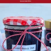 Mixed berry jam in a glass jar with a red and white checkered lid and twine bow.