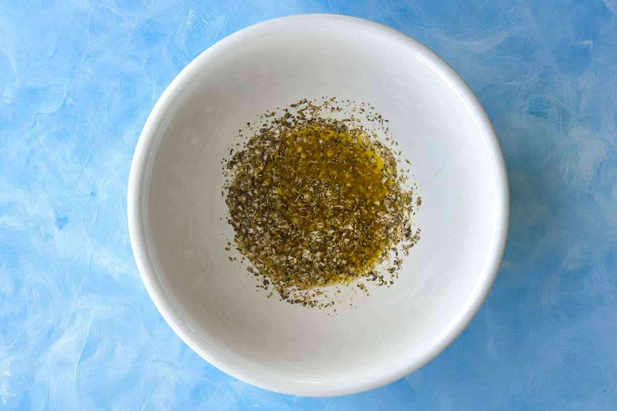 Olive oil, garlic, and Italian seasoning mixed in a bowl for Mediterranean roasted vegetable marinade.