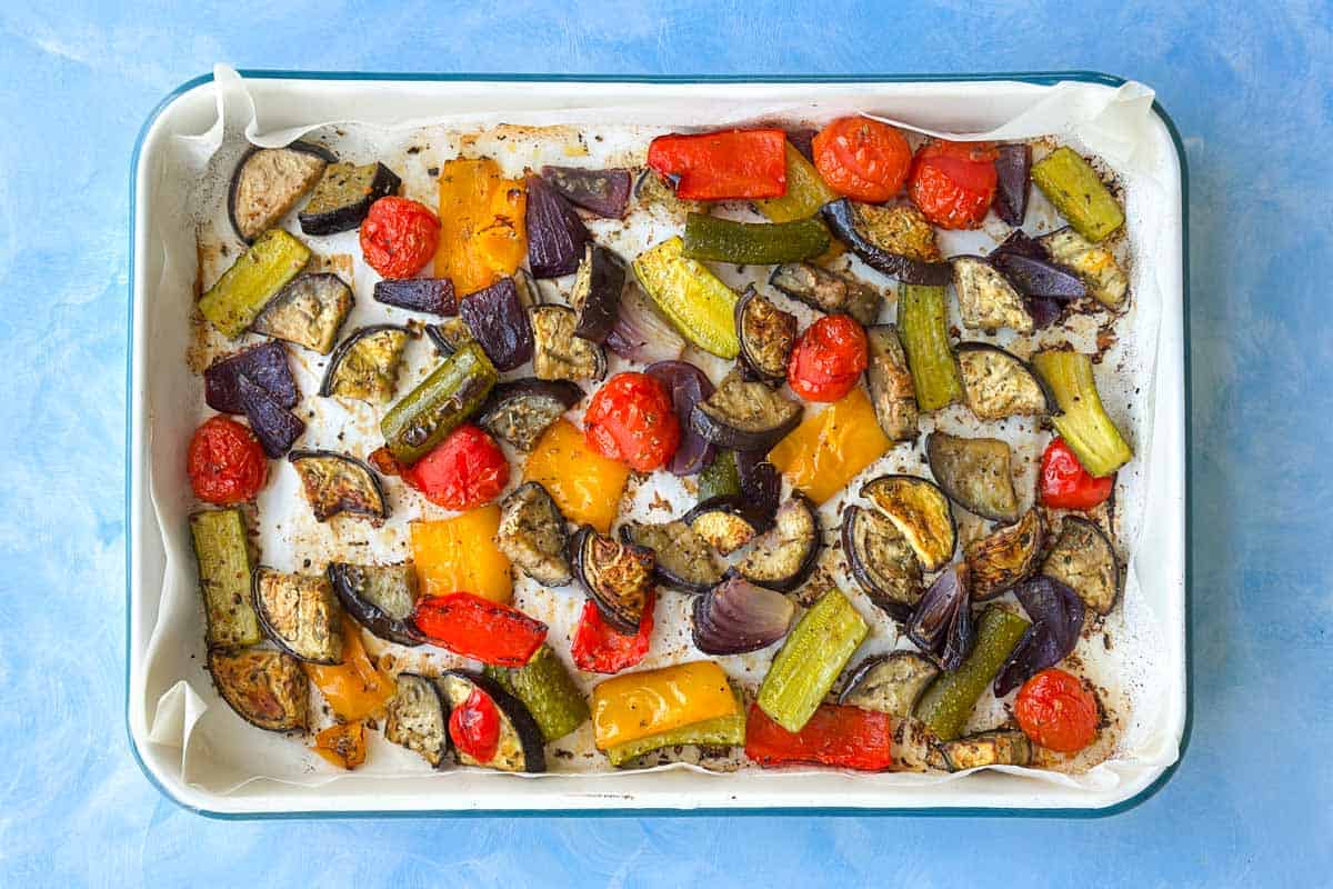 Roasted Mediterranean vegetables in a baking dish with caramelized eggplant, zucchini, peppers, red onion, and cherry tomatoes.