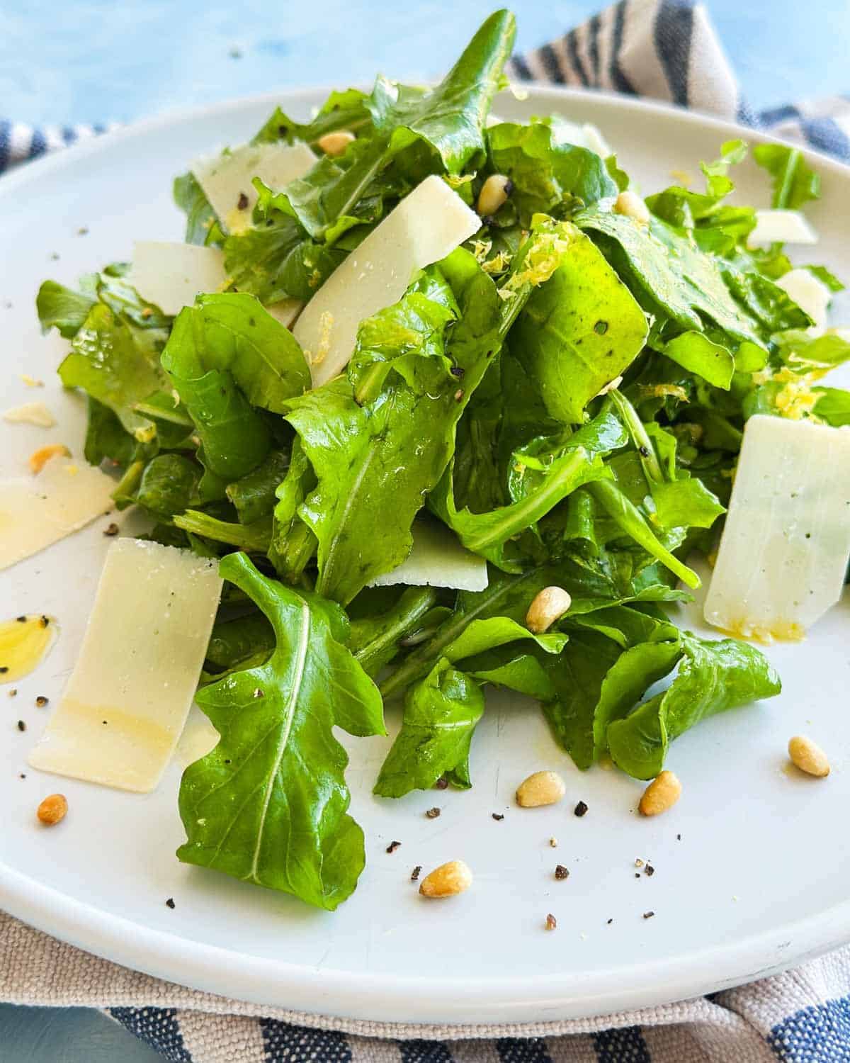 Close-up of rocket salad with arugula leaves, shaved Parmesan, pine nuts, and a drizzle of olive oil.