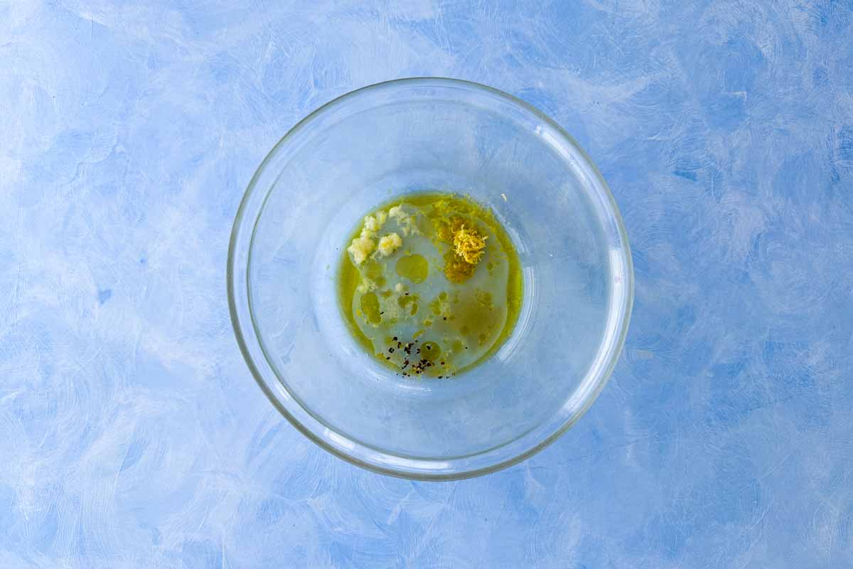 Lemon dressing ingredients in a glass bowl for rocket salad, including olive oil, garlic, lemon, and seasoning.