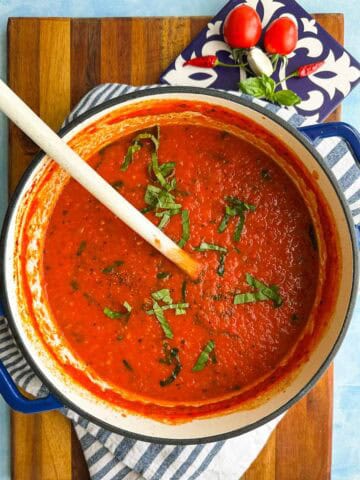 Spicy tomato pasta sauce in a blue Dutch oven with basil, tomatoes, garlic, and chilies styled beside the pot.