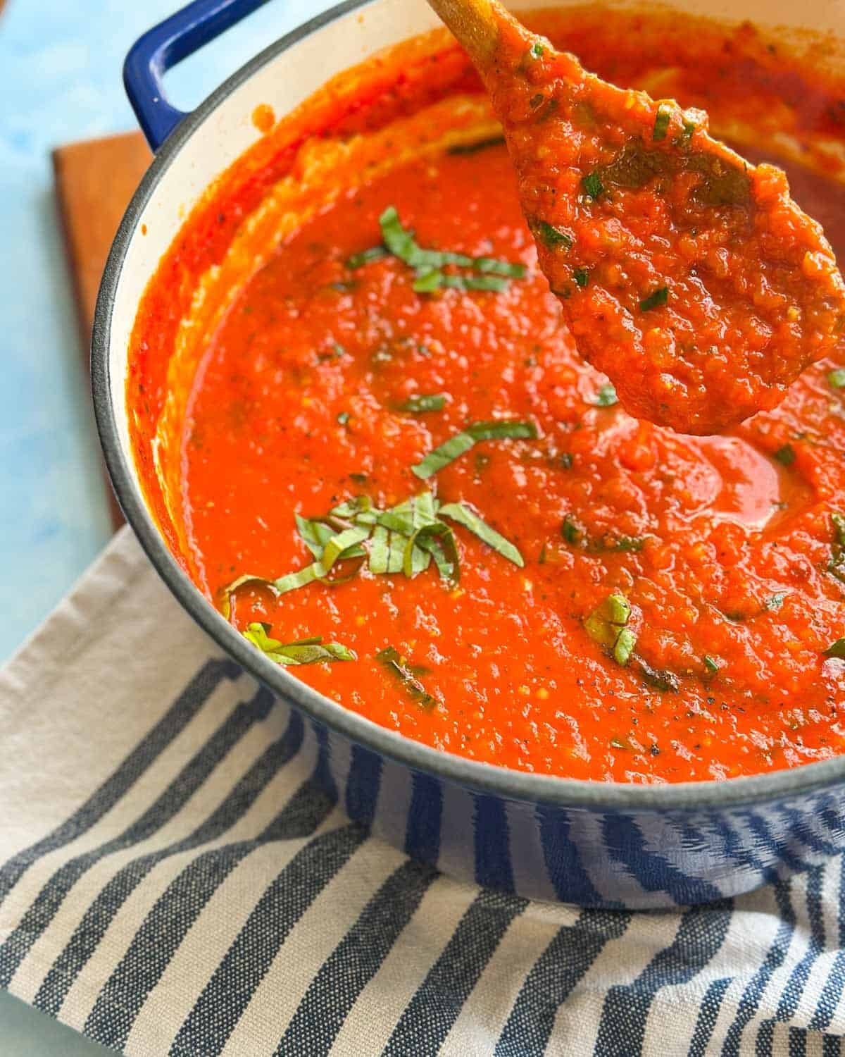 Close-up of a wooden spoon lifting chunky spicy tomato sauce with fresh basil from the pot.