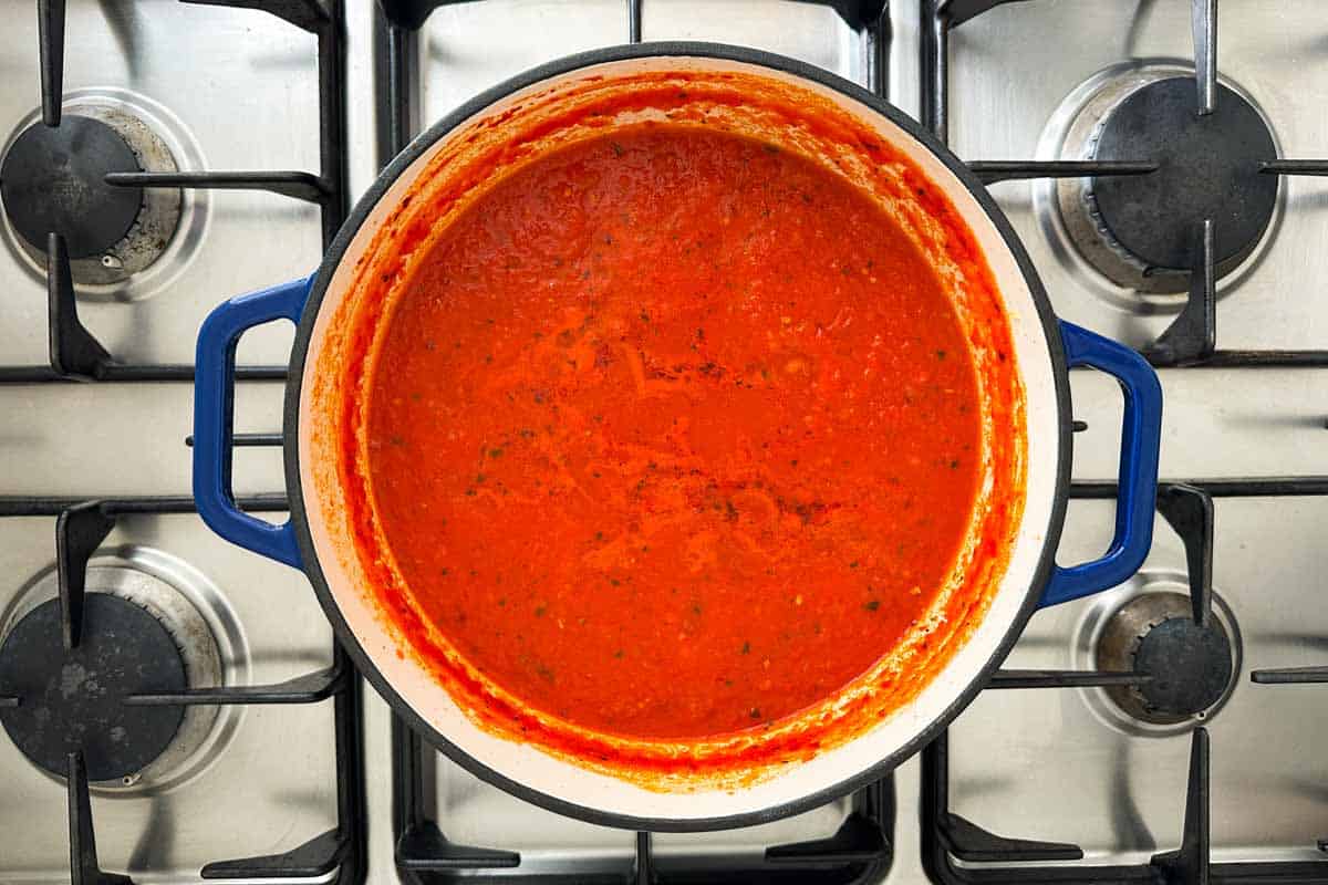 Spicy tomato pasta sauce simmering in a Dutch oven until thick, red, and glossy.