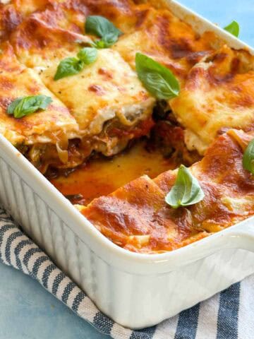 Close side view of Mediterranean vegetable lasagna with a missing slice, showing the creamy layers and roasted vegetable filling.