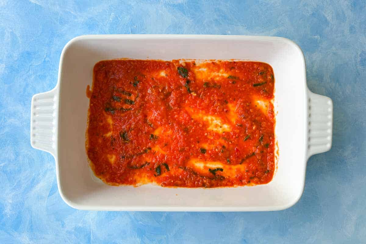 Overhead shot of a baking dish layered with tomato pasta sauce for Mediterranean vegetable lasagna.
