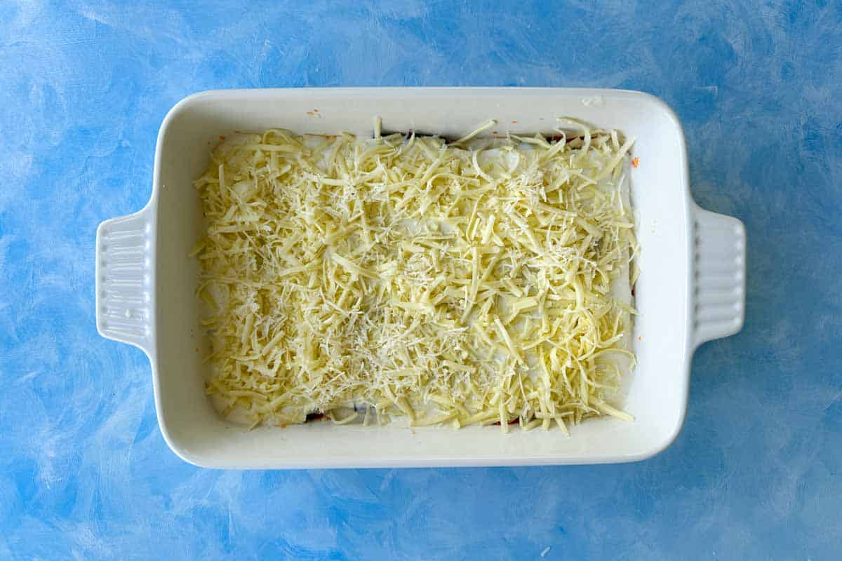 Top-down view of a lasagna layer covered with shredded mozzarella, bechamel sauce and Parmesan cheese.