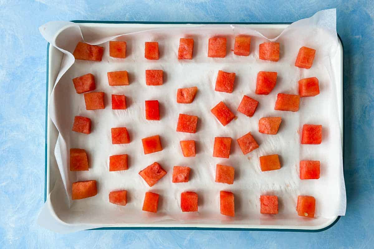 Watermelon cut into small cubes, placed on a baking tray covered with parchment paper, ready to be frozen.