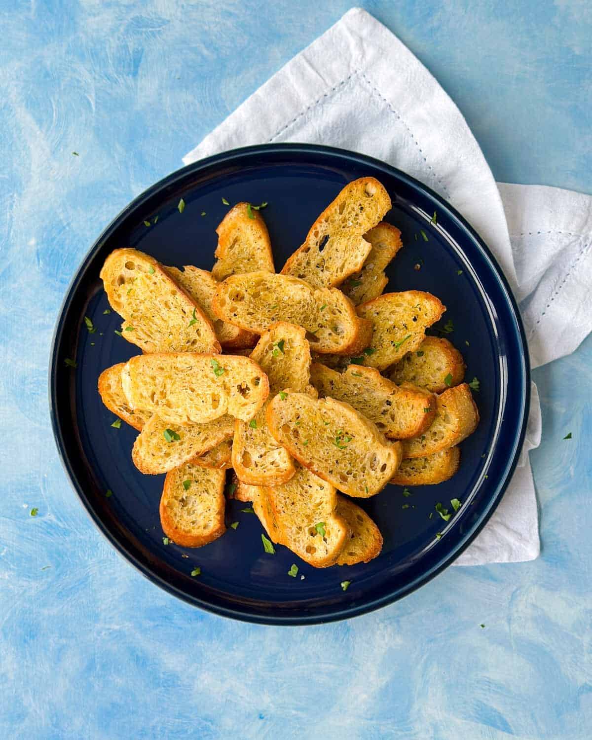 Overhead shot of homemade crostini arranged on a dark blue plate with a white napkin underneath.