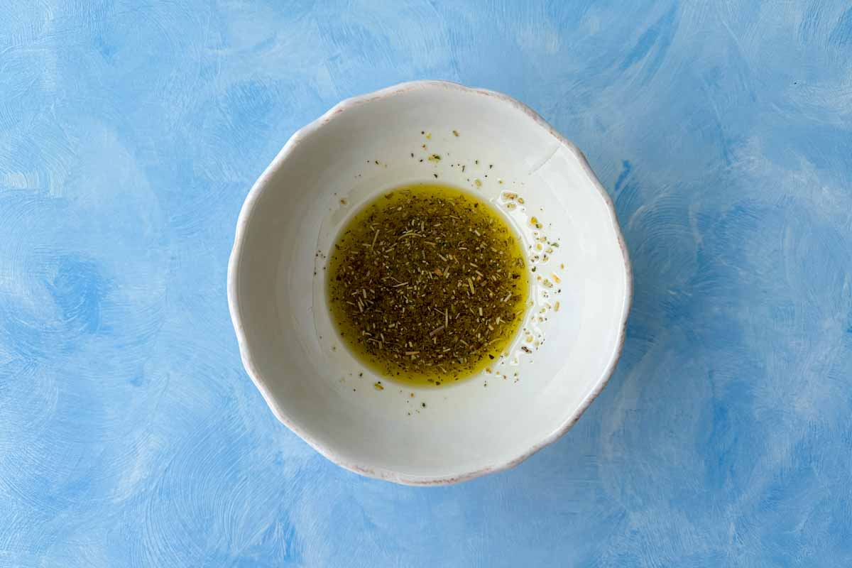Top view of olive oil mixed with Italian seasoning in a white bowl for making homemade crostini.