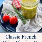 Homemade Dijon vinaigrette in a glass jar with fresh tomatoes and herbs.