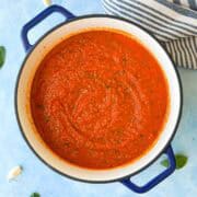 Top view of thick homemade Napolitana sauce in a Dutch oven with a rich red tomato texture and flecks of fresh herbs.