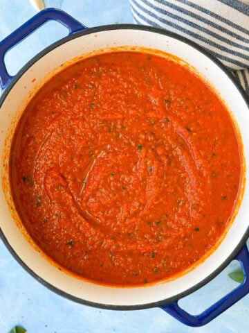 Top view of thick homemade Napolitana sauce in a Dutch oven with a rich red tomato texture and flecks of fresh herbs.