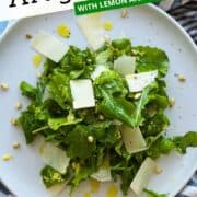 Fresh arugula salad with lemon, parmesan, and olive oil on a white plate.