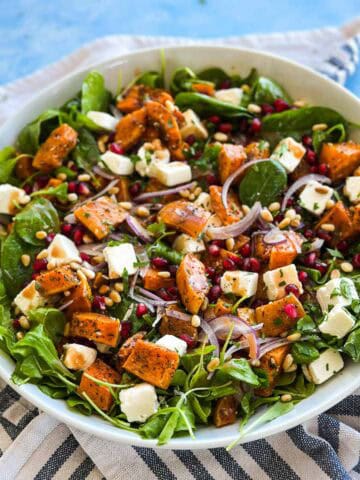 Fresh butternut squash salad with roasted squash, feta cubes, red onion, pomegranate arils, pine nuts, and greens.