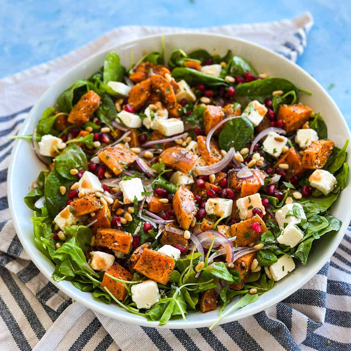 Fresh butternut squash salad with roasted squash, feta cubes, red onion, pomegranate arils, pine nuts, and greens.