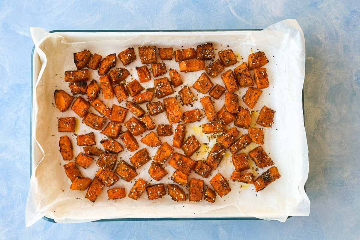 Roasted butternut squash pieces on a parchment-lined tray, golden and lightly browned around the edges.
