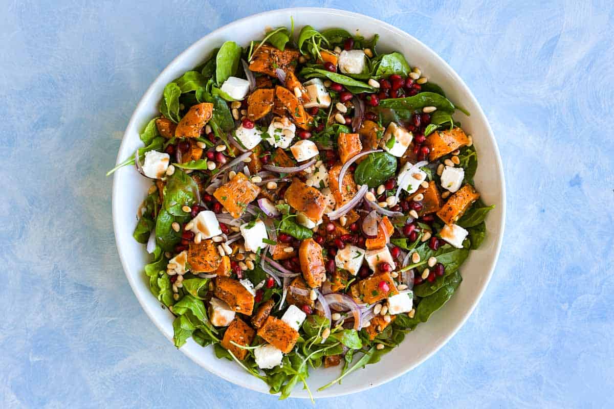 Finished roasted butternut squash salad with feta, pomegranate arils, pine nuts, red onion, and leafy greens.