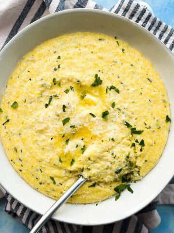 Creamy parmesan polenta with a spoonful scooped out, topped with melted butter, parmesan, and fresh parsley.