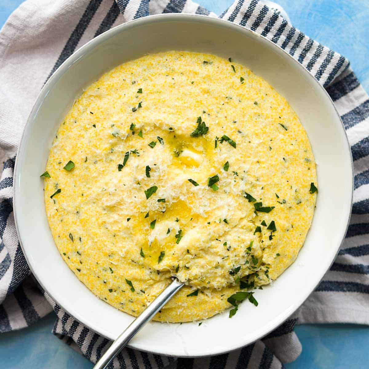 Creamy parmesan polenta with a spoonful scooped out, topped with melted butter, parmesan, and fresh parsley.