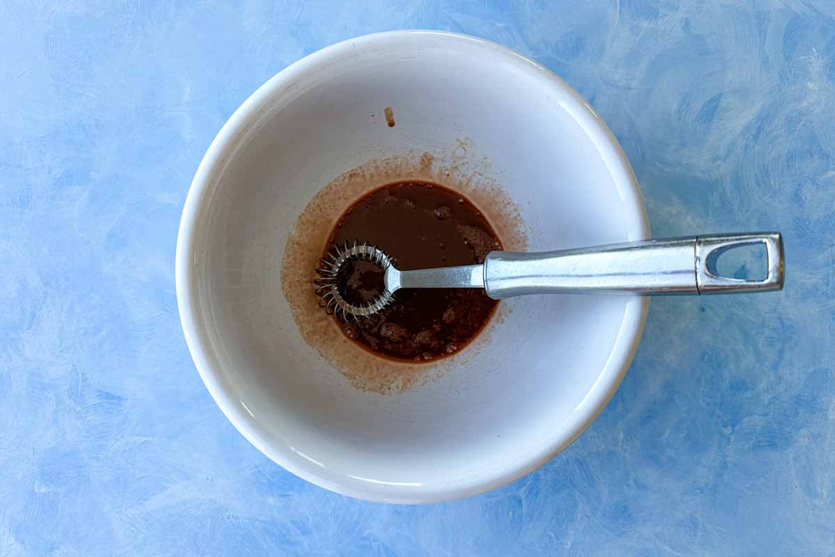 Overhead process image of pomegranate molasses dressing ingredients in a white bowl with a small whisk.
