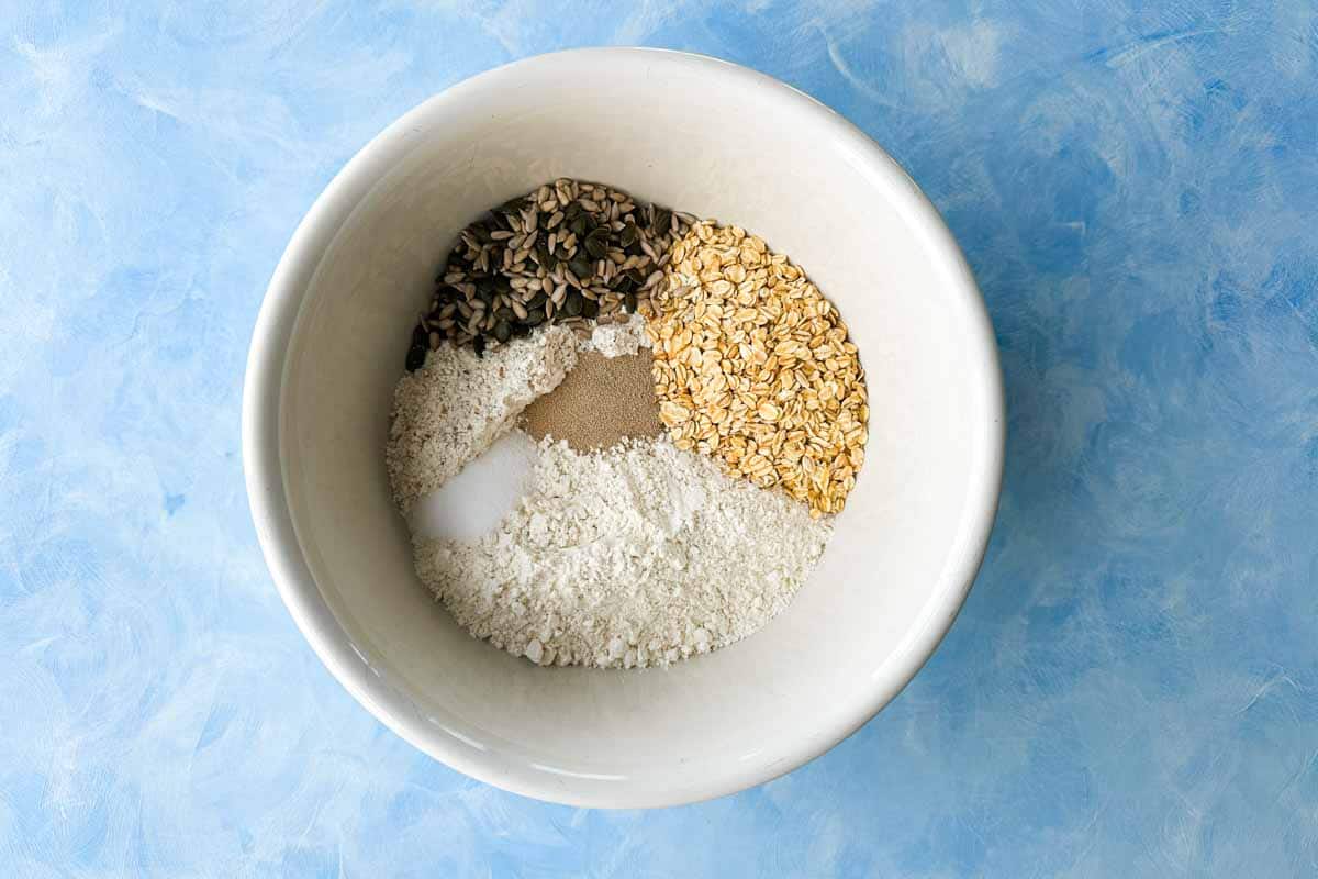 Flour, oats, mixed seeds, yeast, and salt arranged in a mixing bowl before combining.