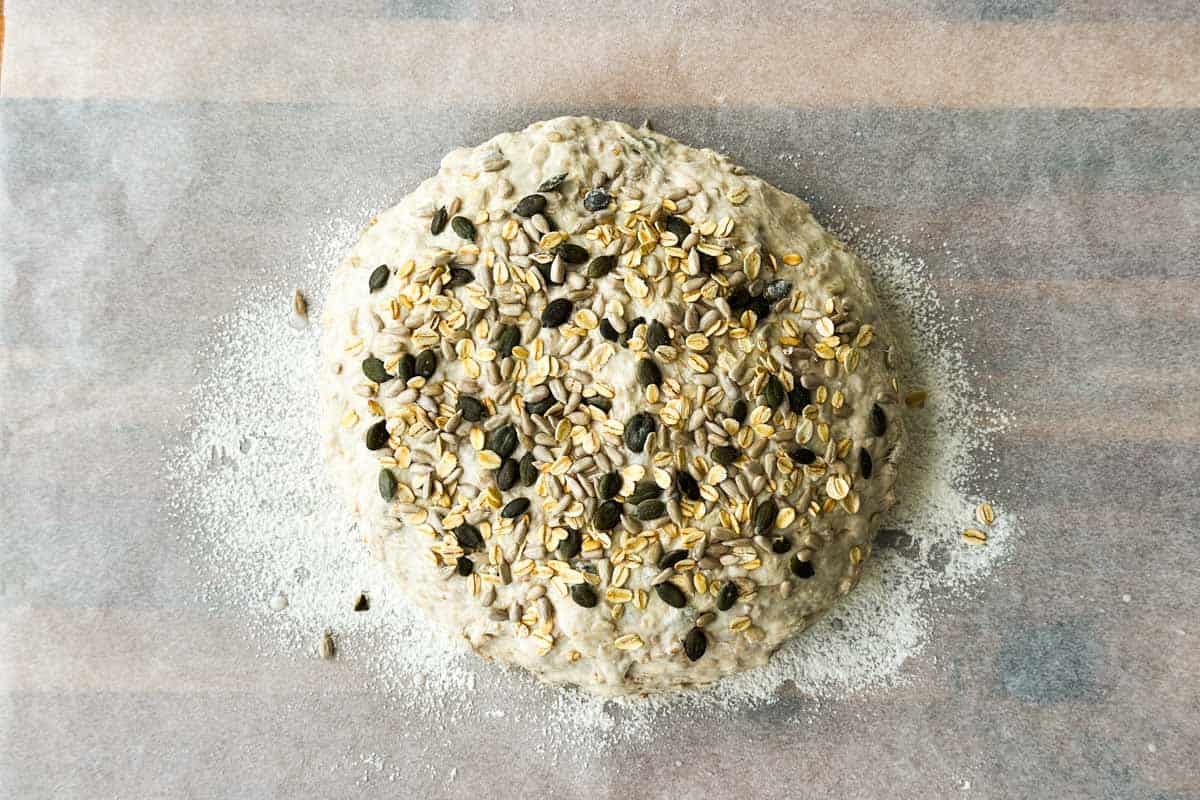 Unbaked dough topped with oats and seeds on parchment paper.